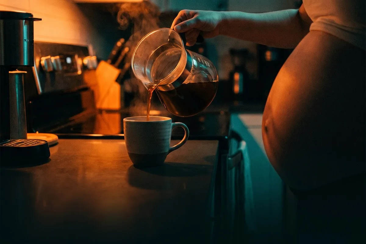 Gestante servindo café filtrado numa xícara, na cozinha, à noite